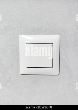 On a light gray wall, there's a square white electric light switch. Interior equipment: press the power button. Stock Photo