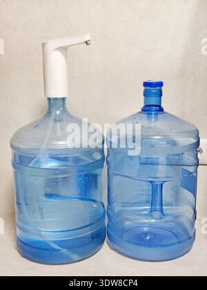Two large blue water bottles standing side by side, one with an electric water pump on top. Clear plastic containers used for drinking water, placed i Stock Photo