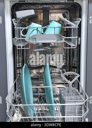 Open dishwasher with clean turquoise cups and plates neatly arranged inside. Modern kitchen appliance interior with stainless steel and organized dish Stock Photo
