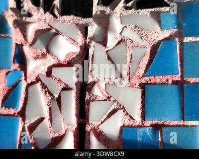 Close-up of a colorful mosaic made of blue, white, and black ceramic tiles with visible cracks and pink grout texture in sunlight Stock Photo