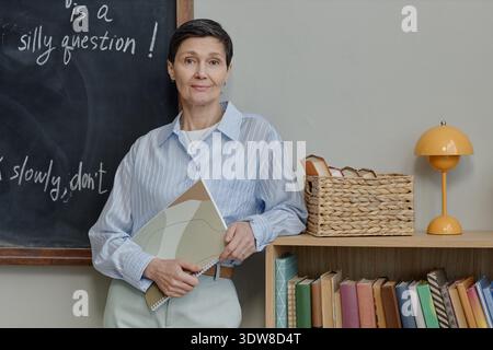 Portrait of Middle Aged Caucasian Woman Standing in Classroom Holding Notebook Stock Photo