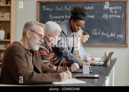 Young Black Woman Instructing Senior Caucasian Men Using Laptop in Classroom Stock Photo