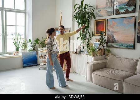 Happy married couple of artists lively discussing artworks hang on wall exhibition at home gallery. Stock Photo