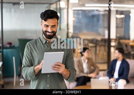 Smiling Middle Eastern businessman working on digital tablet in office Stock Photo