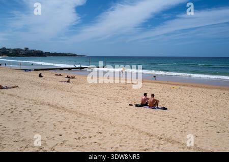 Two men sitting together on a vast sandy beach looking out at the ocean in a popular coastal area. Stock Photo