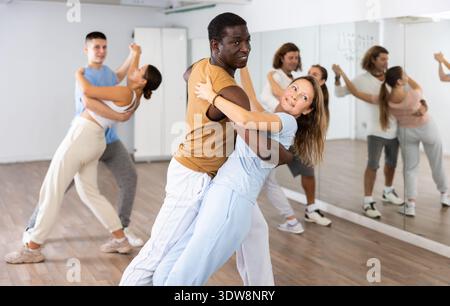 Cheerful diverse young adult people dancing together active expressive dances in pairs in modern class Stock Photo