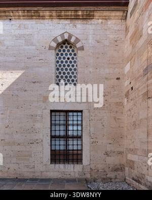 Mevlana Museum exterior detail: travertine wall with an arched window of circular panes and a rectangular barred window, Konya, Turkey Stock Photo