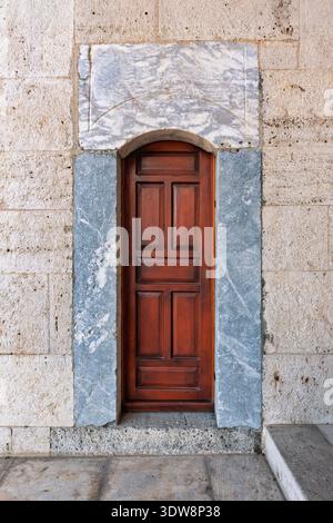 Arched dark wood door framed by veined blue marble and porous limestone blocks, historic architectural detail, Turkey Stock Photo