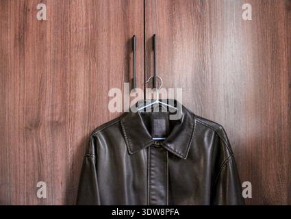 Dark brown retro style leather jacket is hanging on the handle of the wardrobe. Stock Photo