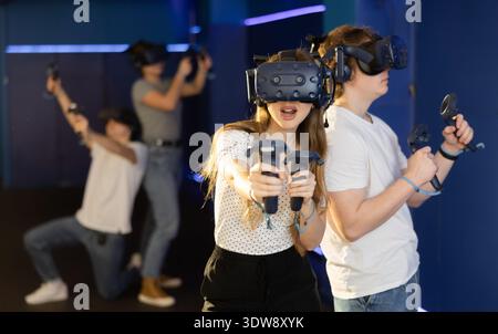 Portrait of woman using virtual reality goggles controlling joysticks standing in dark room Stock Photo