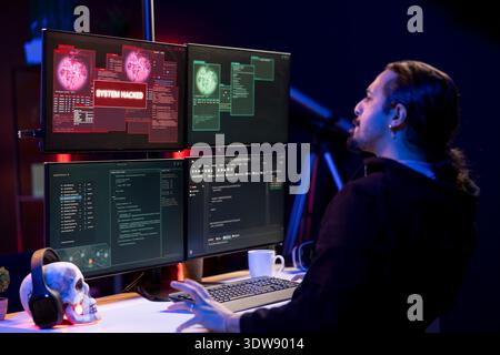 Hacker doing covert operations in secret hideaway to bypass advanced security barriers. Rogue programmer in neon apartment engineering data theft script to penetrate firewalls using PC Stock Photo