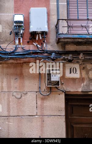 Fiber optic boxes and electrical wiring mounted on an ancient stone wall of a old residential building, showing the contrast between modern technology Stock Photo