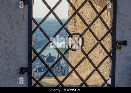 SALZBURG, AUSTRIA - JULY 5, 2015: Salzburg historic old town seen through a window-like opening in the wall of Hohensalzburg Fortress, with a metal gr Stock Photo
