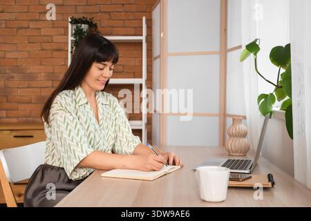 Beautiful woman writing in notebook on table at home Stock Photo