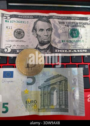 High angle shot of a Bitcoin token symbol standing over paper currency on a laptop. Conceptual image of the fight for dominance between decentralized Stock Photo