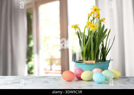 Easter eggs on table and daffodils against blurred window. Space for text Stock Photo