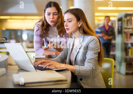 Two female students studying in library with books and laptop Stock Photo