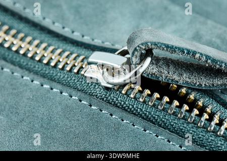 Detailed view of a silver metal zipper slider on textured blue suede leather fabric material Stock Photo