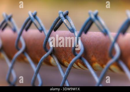 Close-up of rusty chain link fence with intertwined wires and weathered metal texture, selective focus on links Stock Photo