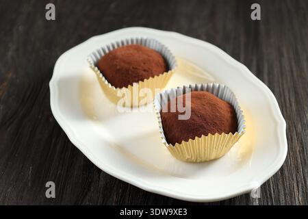 Dubai Chewy Chocolate with Gold Paper Liner on White Oval Plate, Chocolate Coating Mochi Japanese Food Dessert. Isolated on the Black Wooden Table Stock Photo