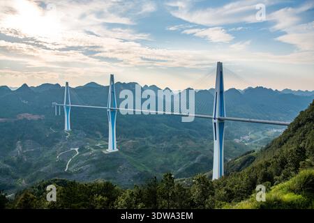 The Pingtang Grand Bridge in Guizhou Province, China, stands majestically over a lush mountainous landscape during sunset. Stock Photo