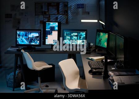 Empty modern security control room featuring multiple surveillance monitors displaying live camera feeds from various locations, ergonomic chairs positioned in front of workstations Stock Photo