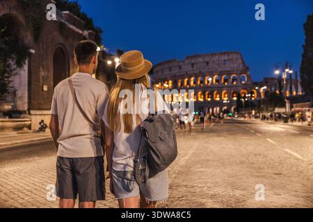 Young couple standing together and admiring the illuminated Colosseum at night in Rome, Italy Stock Photo