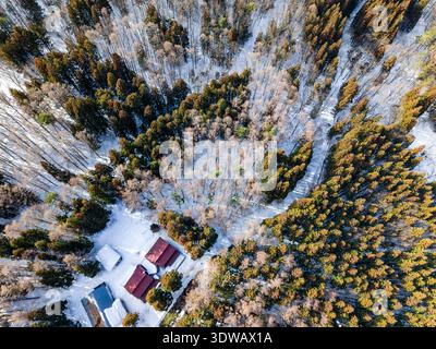 Scenic winter landscape featuring dense forest and small cabins from above Stock Photo
