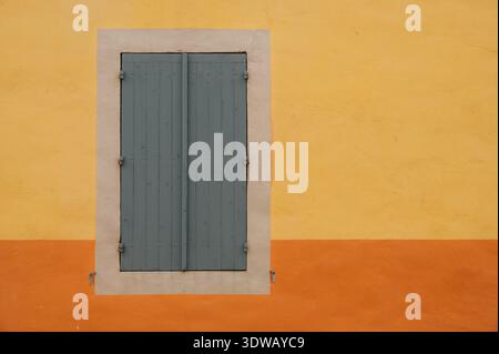 Colorful Mediterranean house facade with closed blue wooden shutters on yellow and orange wall, minimalist architectural background Stock Photo