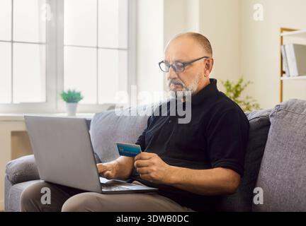 Elderly senior man pays online with credit card while using laptop at home Stock Photo