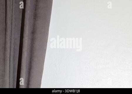 A soft gray fabric curtain with vertical pleats is positioned on the left, obscuring a portion of a white wall with a subtle, uneven texture Stock Photo