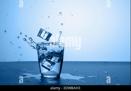 Glass of water with splash and ice cube on trend classic blue background Stock Photo