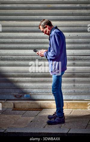 Thin man standing on pavement looking at smartphone - Loches, Indre-et-Loire (37), France. Stock Photo