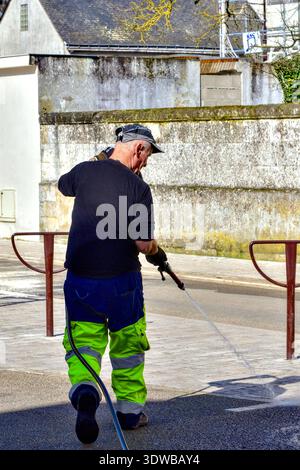 Council worker washing down pavement with hosepipe after weekend market has cleared - Loches, Indre-et-Loire (37), France. Stock Photo