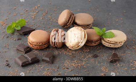 French sweet cocoa and vanilla cookies macarons macaroons with crumbs, mint and chocolate pieces on dark grey stone background. Pastry shop card. Stock Photo