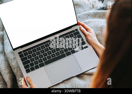 Close-up of a modern laptop with blank white screen held in hands while sitting on a cozy bed. Ideal mockup for website design, online marketing, remo Stock Photo