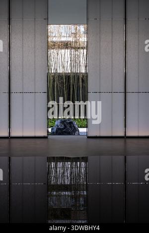 Vertical detail shot focusing on the reflection of a bamboo garden and stone rock in the shallow water of a modern interior space. Stock Photo