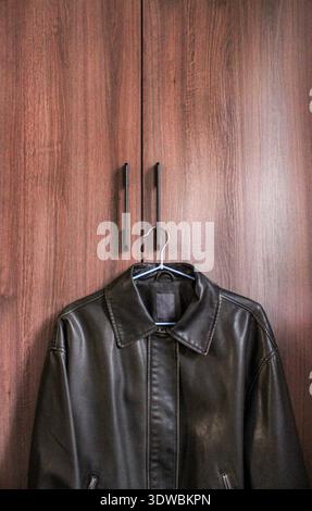 Dark brown retro style leather jacket is hanging on the handle of the wardrobe. Stock Photo