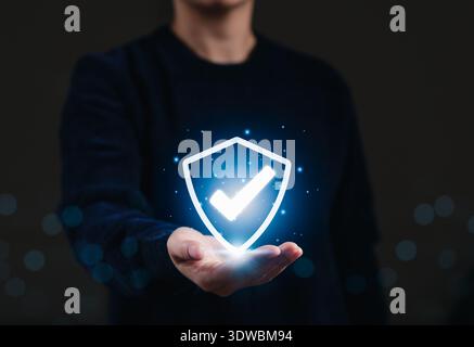 Cybersecurity protection concept with shield and checkmark icon above hand, symbolizing data protection, secure access, privacy compliance and trusted Stock Photo