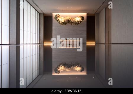 Modern architectural interior showing a perfectly symmetrical hallway with high-end materials, a reflective floor, and a warm glowing sculpture at the Stock Photo