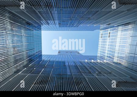 Abstract architectural shot looking up at the vertical lines and glass surfaces of modern skyscrapers, creating a geometric composition with the sky. Stock Photo