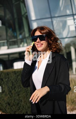 Young businesswoman smiling while talking on smartphone outdoors, showing positive mood and successful business lifestyle. Stock Photo