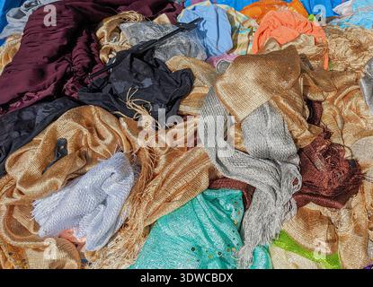 Heap of shimmering woven fabrics in gold, silver, turquoise, black and burgundy tones, visible metallic threads and mesh textures, folded and crumpled Stock Photo