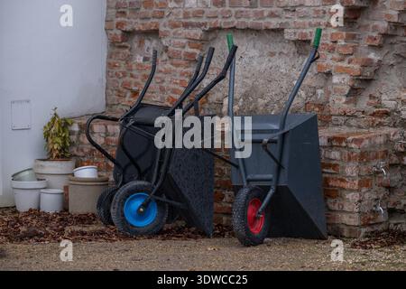 Garden Wheelbarrows Standing Near Brick Wall in Backyard Stock Photo