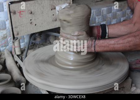 Indian artisan forms a clay pot on a fast‑spinning potters' wheel in Delhi, India, showing traditional pottery making (New Delhi 2019). Stock Photo