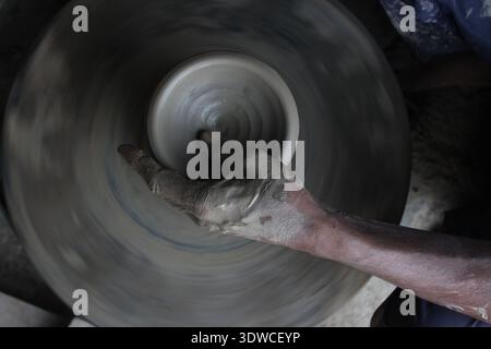 Indian artisan forms a clay pot on a fast‑spinning potters' wheel in Delhi, India, showing traditional pottery making (New Delhi 2019). Stock Photo