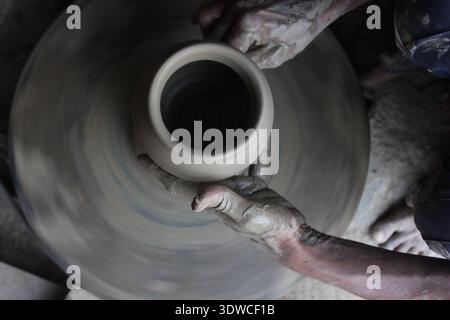 Indian artisan forms a clay pot on a fast‑spinning potters' wheel in Delhi, India, showing traditional pottery making (New Delhi 2019). Stock Photo
