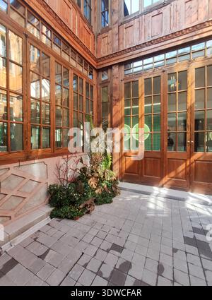 An outdoor perspective of a private courtyard featuring high-quality wooden glass doors and windows, reflecting natural sunlight on a stone floor. Stock Photo