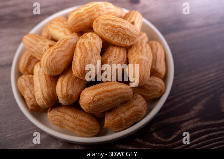close-up of a ceramic bowl overflowing with golden-brown mini eclairs on a dark wooden table; warm soft lighting accentuates ridged choux texture and Stock Photo