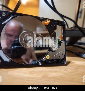 Close-up view of an internal computer hard disk drive HDD with the top cover removed, exposing the mirror-like platters. A technician is visibly refle Stock Photo